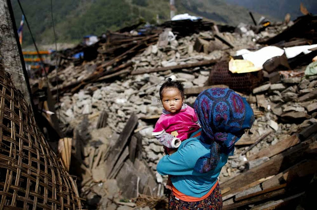 Mother holding a baby overlooking their destroyed home